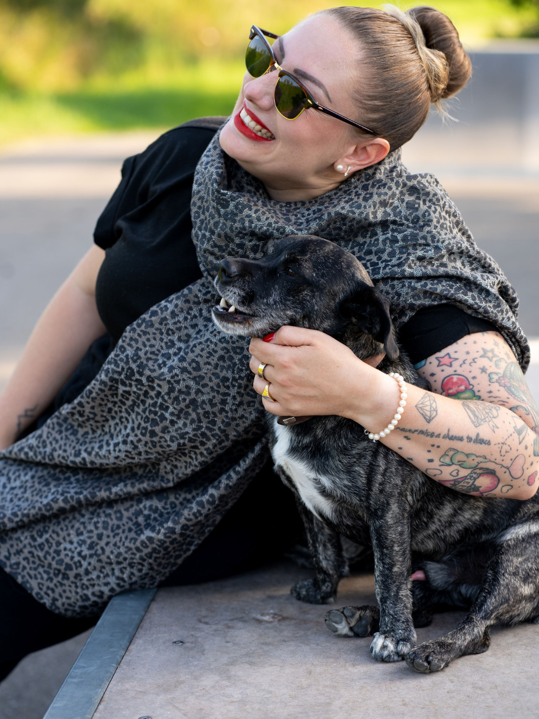Leo Design Schal um den Hals einer blonden Frau. Neben ihr sitzt ein Hund
