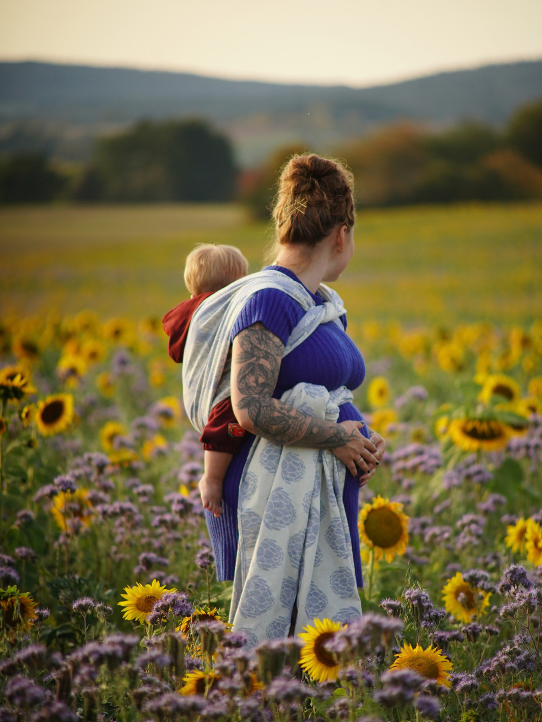 Die Mutter hat beide Hände auf ihrem Babybauch. Das Kind ist auf dem Rücken eingebunden in Camilou Seren Sky